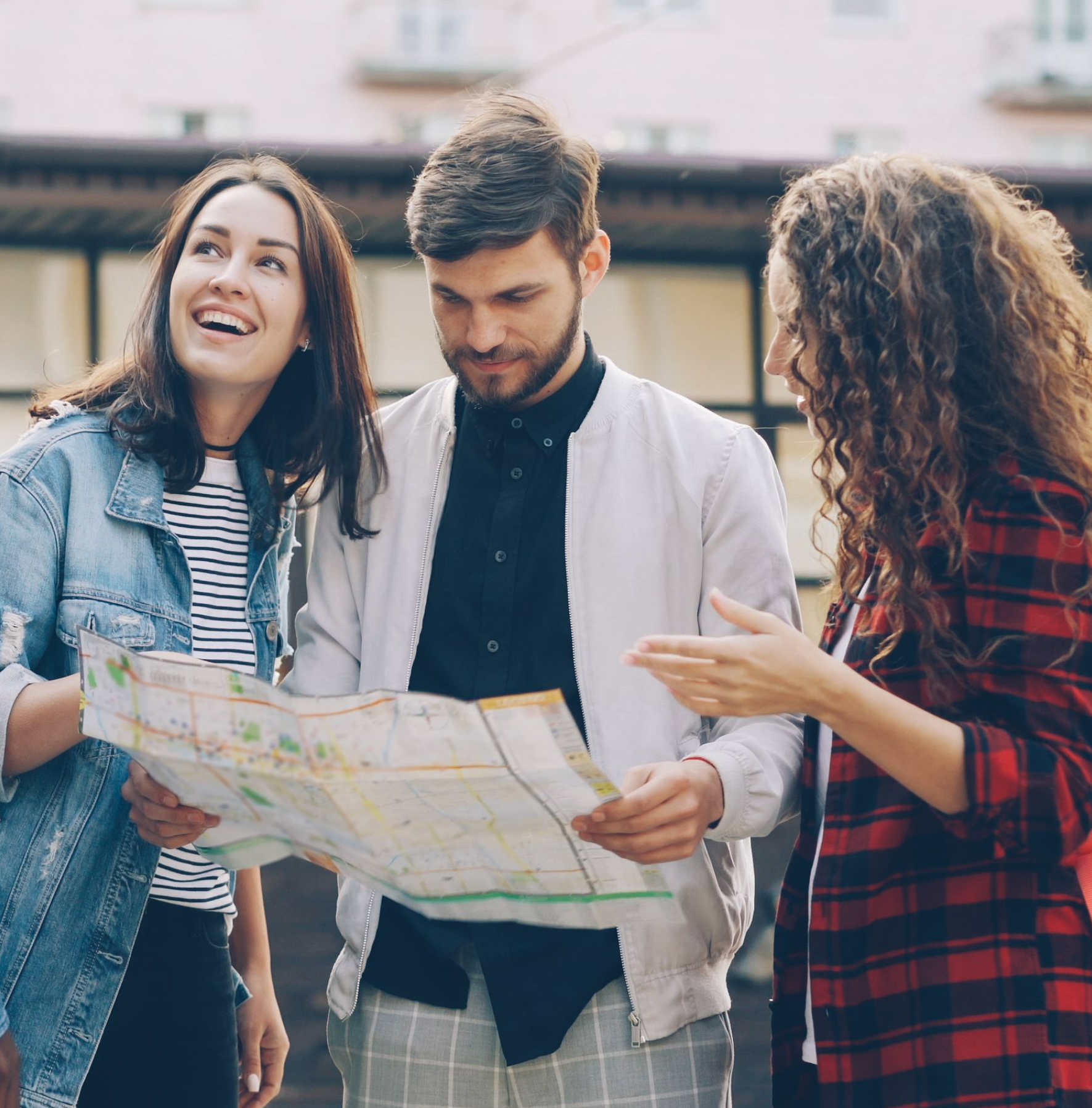 Three young adults looking at and discussing a city map outdoors in casual clothes.